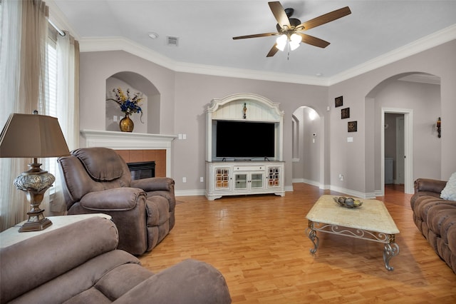 living room with a tiled fireplace, ornamental molding, ceiling fan, and light wood-type flooring