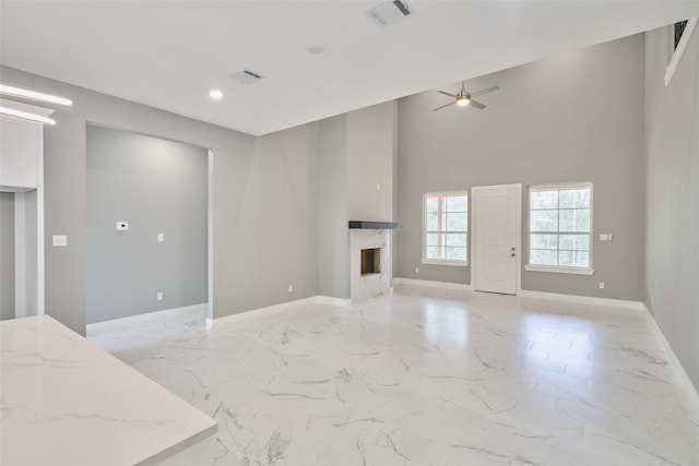 living room with a high ceiling, a premium fireplace, and ceiling fan