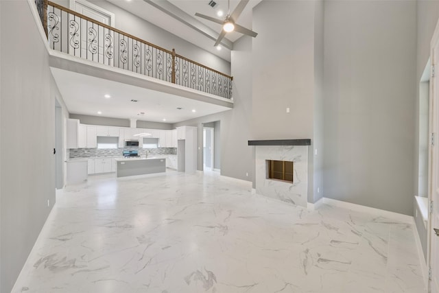 110 Broken Wheel Cir, Conroe, TX 77316 - unfurnished living room featuring a towering ceiling, ceiling fan, light marble finish floors, baseboards, and a high end fireplace