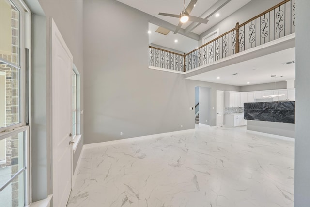 unfurnished living room with a high ceiling, a ceiling fan, recessed lighting, and marble finish floor