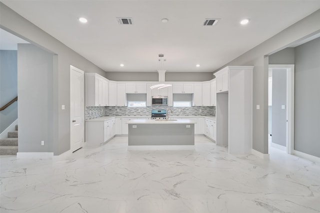 kitchen with visible vents, decorative backsplash, an island with sink, a sink, and appliances with stainless steel finishes