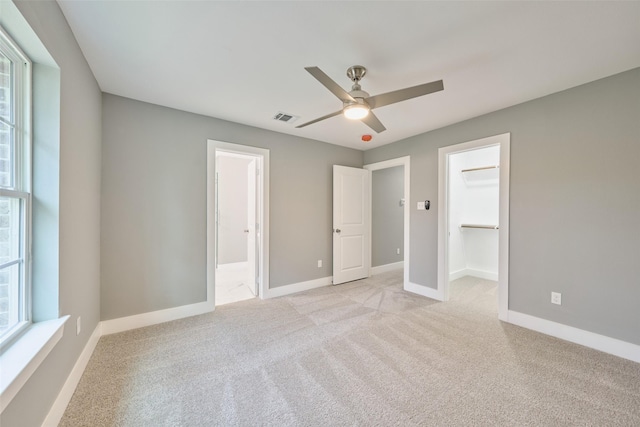 unfurnished bedroom featuring ensuite bathroom, a walk in closet, ceiling fan, light carpet, and a closet