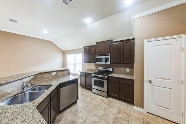 kitchen with lofted ceiling, sink, light stone counters, dark brown cabinets, and appliances with stainless steel finishes