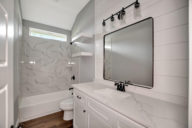 full bathroom featuring hardwood / wood-style floors, vanity, tiled shower / bath, vaulted ceiling, and toilet