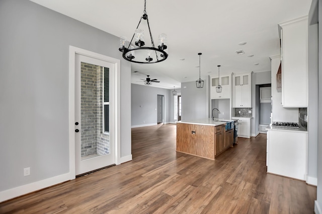 kitchen with pendant lighting, dark wood-type flooring, a kitchen island with sink, backsplash, and white cabinets