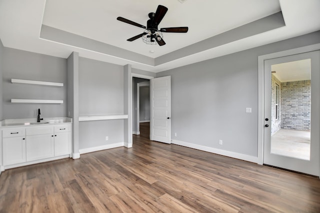 unfurnished bedroom with ceiling fan, sink, a tray ceiling, and hardwood / wood-style floors