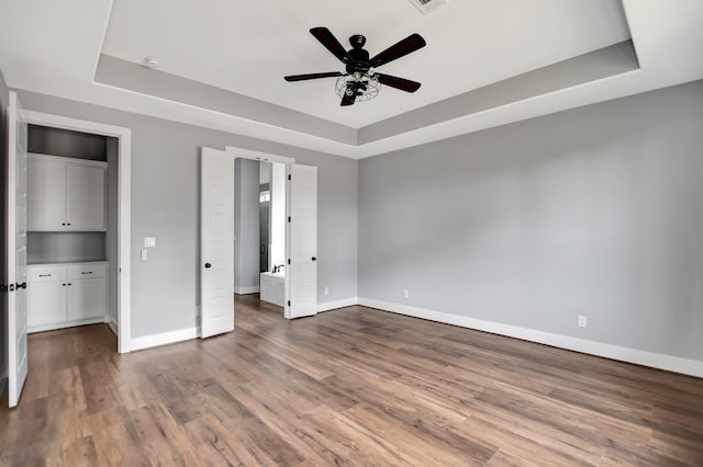 unfurnished bedroom featuring wood-type flooring, ceiling fan, and a tray ceiling