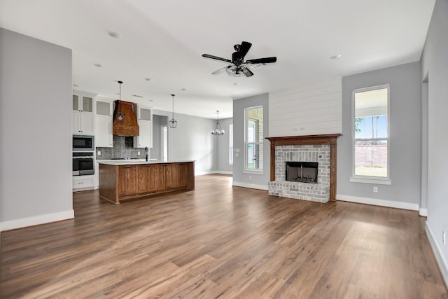 unfurnished living room featuring sink, dark hardwood / wood-style floors, ceiling fan with notable chandelier, and a brick fireplace