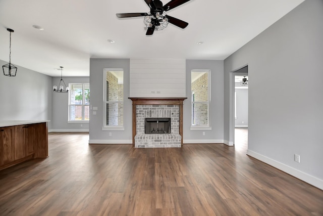 unfurnished living room featuring dark hardwood / wood-style flooring, ceiling fan with notable chandelier, and a fireplace