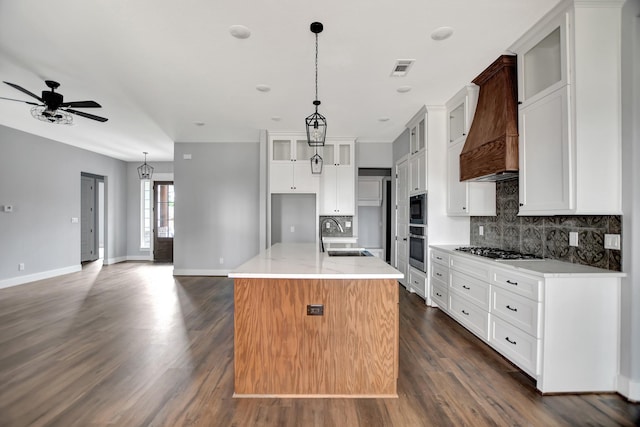 kitchen with sink, premium range hood, black microwave, an island with sink, and stainless steel gas stovetop