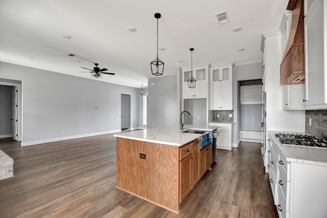 kitchen featuring an island with sink, sink, white cabinets, stainless steel gas cooktop, and light stone counters