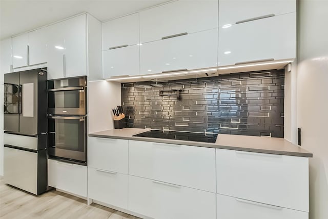 kitchen featuring stainless steel appliances, light hardwood / wood-style flooring, white cabinets, and decorative backsplash