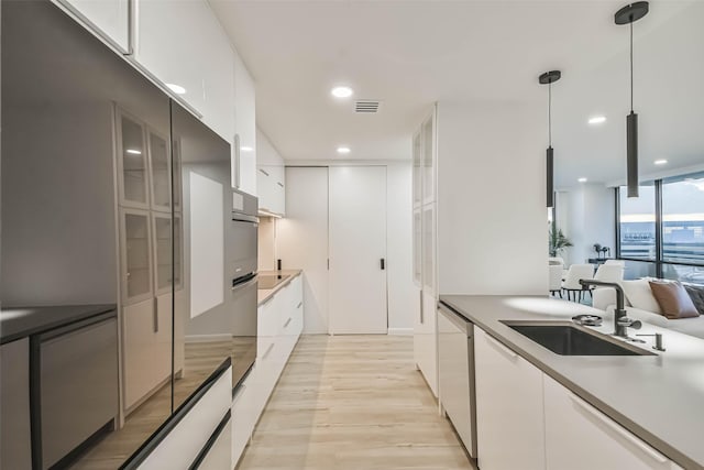 kitchen with pendant lighting, sink, dishwasher, light hardwood / wood-style floors, and white cabinets