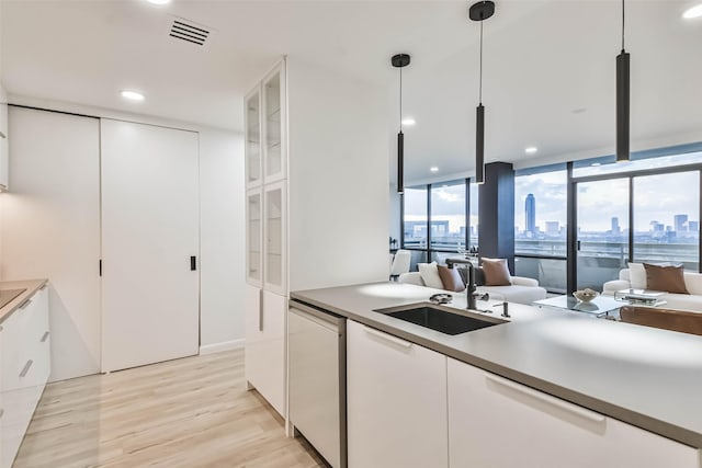 kitchen featuring sink, white cabinetry, decorative light fixtures, light wood-type flooring, and dishwasher