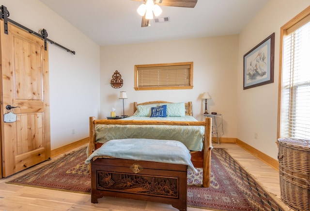 bedroom featuring ceiling fan, a barn door, and light wood-type flooring