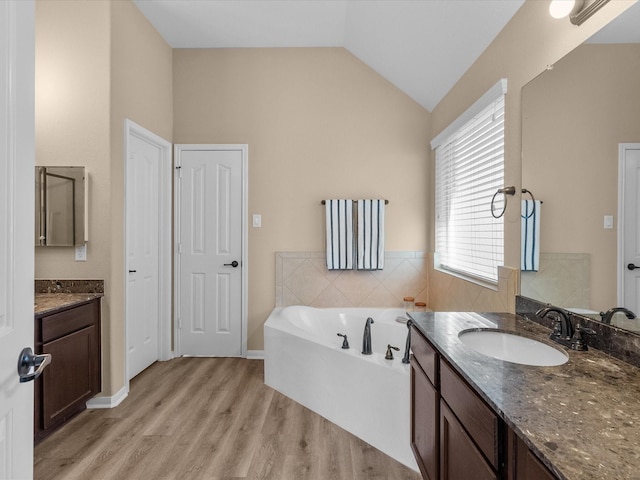 bathroom with vaulted ceiling, wood-type flooring, vanity, and a bathtub