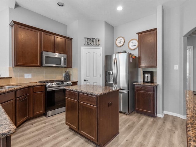 kitchen featuring stainless steel appliances, a kitchen island, dark stone countertops, and light hardwood / wood-style flooring