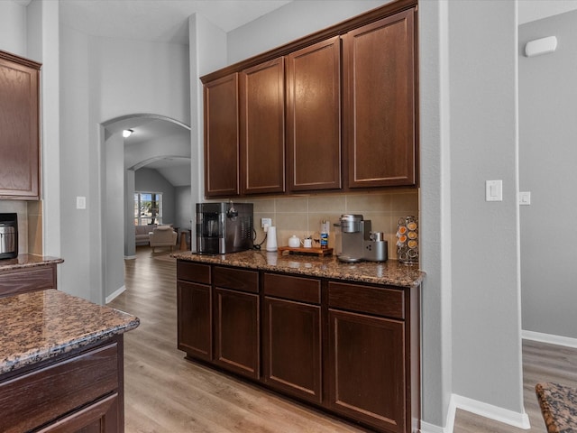 kitchen featuring dark brown cabinetry, dark stone countertops, light hardwood / wood-style floors, and backsplash