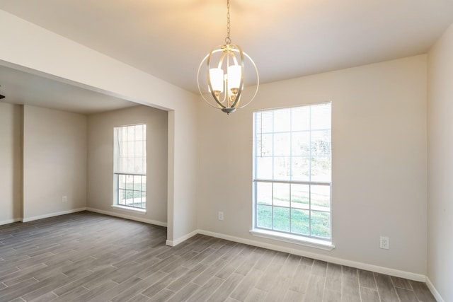 unfurnished room featuring a wealth of natural light, a notable chandelier, and light hardwood / wood-style flooring