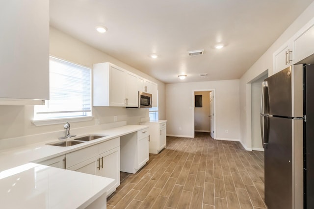 kitchen featuring appliances with stainless steel finishes, light hardwood / wood-style floors, sink, and white cabinets