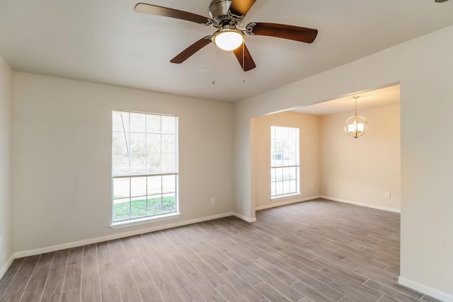 unfurnished room featuring ceiling fan with notable chandelier, a wealth of natural light, and light wood-type flooring