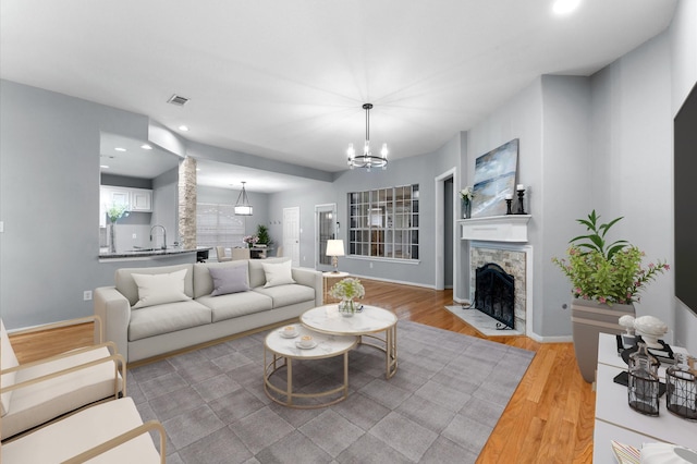 living room with a fireplace, light hardwood / wood-style floors, sink, and a notable chandelier