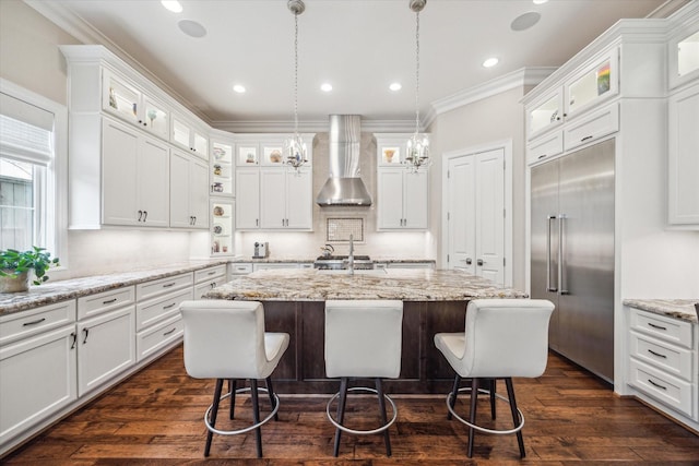 kitchen featuring wall chimney exhaust hood, built in refrigerator, a kitchen island with sink, and white cabinets