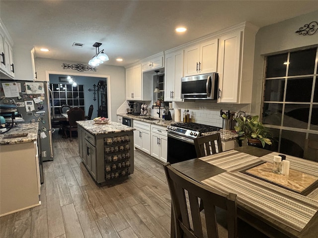 kitchen with a kitchen island, hardwood / wood-style floors, white cabinets, light stone counters, and stainless steel appliances