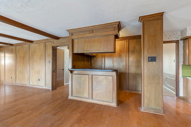 kitchen with a textured ceiling, wood walls, beamed ceiling, and light wood-type flooring