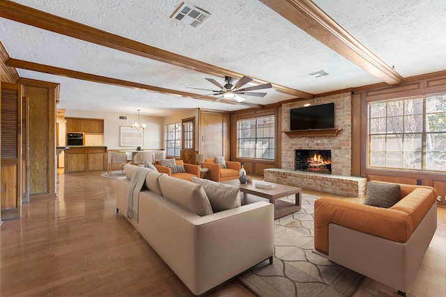 living room featuring light hardwood / wood-style flooring, beam ceiling, a fireplace, a textured ceiling, and ceiling fan with notable chandelier