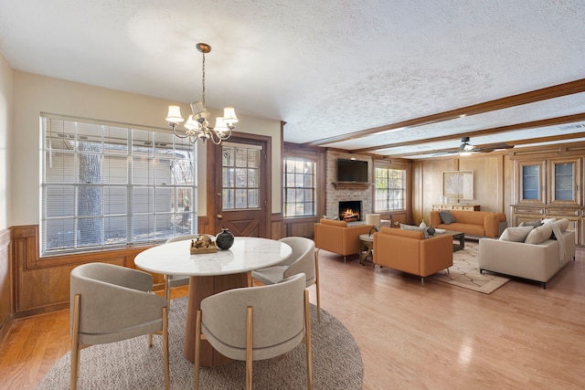 dining area featuring an inviting chandelier, beamed ceiling, a large fireplace, a textured ceiling, and light wood-type flooring