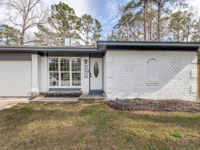 doorway to property with a garage, a lawn, and brick siding