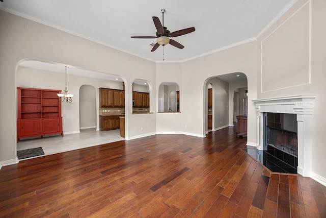 unfurnished living room featuring a tiled fireplace, ceiling fan with notable chandelier, ornamental molding, and dark hardwood / wood-style floors