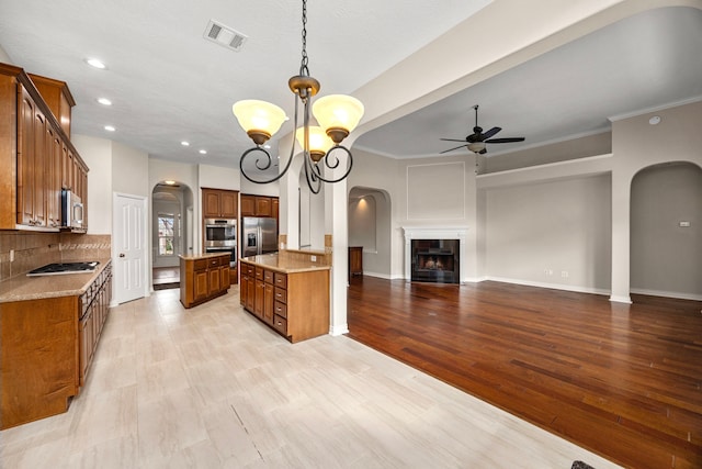 kitchen featuring pendant lighting, ceiling fan with notable chandelier, appliances with stainless steel finishes, light hardwood / wood-style floors, and decorative backsplash