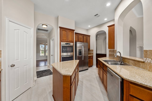 kitchen with sink, a center island, kitchen peninsula, stainless steel appliances, and light stone countertops