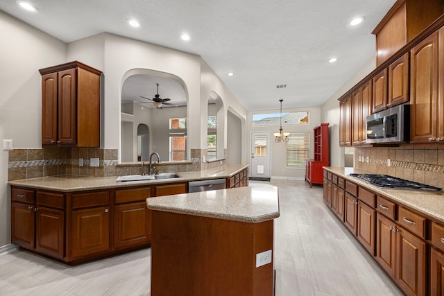 kitchen with sink, appliances with stainless steel finishes, a kitchen island, pendant lighting, and ceiling fan with notable chandelier