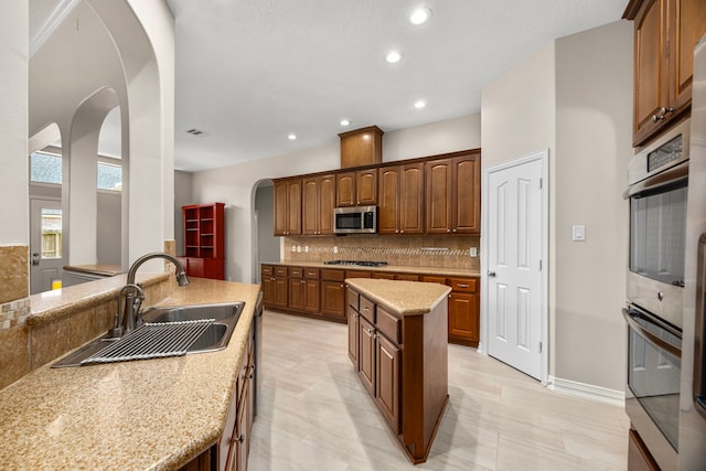 kitchen featuring sink, light stone counters, tasteful backsplash, a center island, and appliances with stainless steel finishes