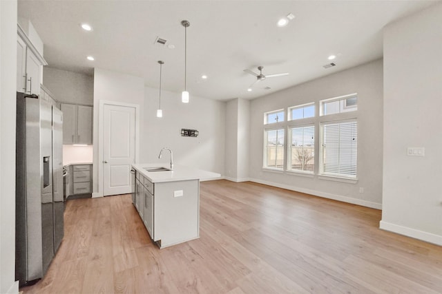 kitchen featuring stainless steel refrigerator with ice dispenser, sink, decorative light fixtures, a center island with sink, and light wood-type flooring