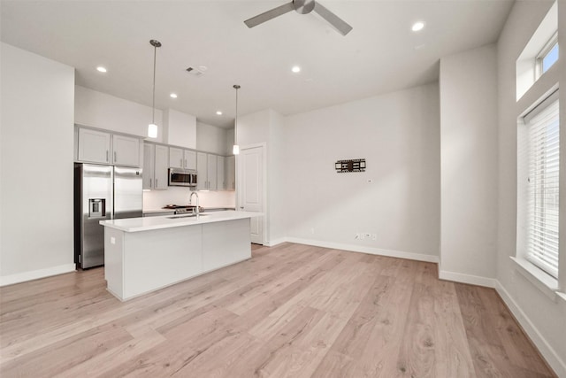 kitchen featuring a center island with sink, light hardwood / wood-style flooring, pendant lighting, ceiling fan, and stainless steel appliances