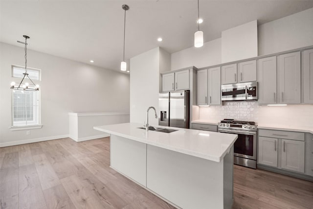 kitchen featuring sink, gray cabinets, hanging light fixtures, stainless steel appliances, and an island with sink