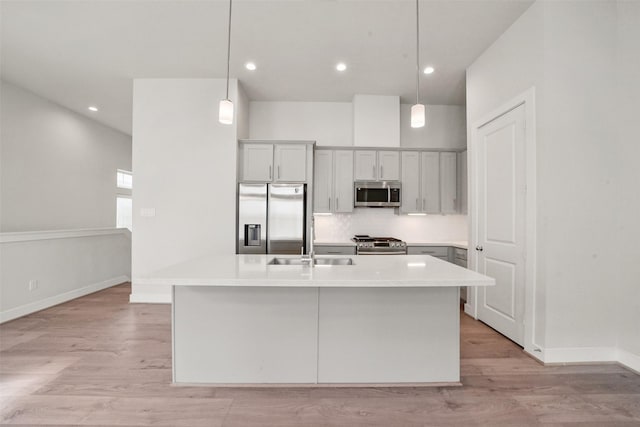 kitchen featuring decorative light fixtures, an island with sink, sink, stainless steel appliances, and light wood-type flooring