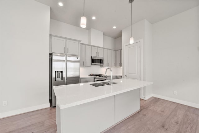 kitchen featuring sink, decorative light fixtures, stainless steel appliances, and a center island with sink