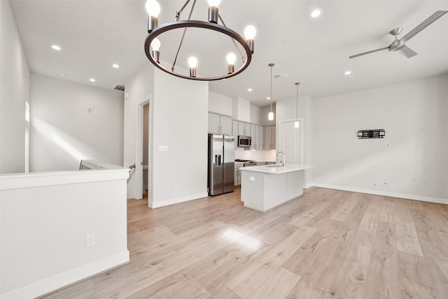 kitchen featuring sink, appliances with stainless steel finishes, white cabinets, a center island with sink, and decorative light fixtures