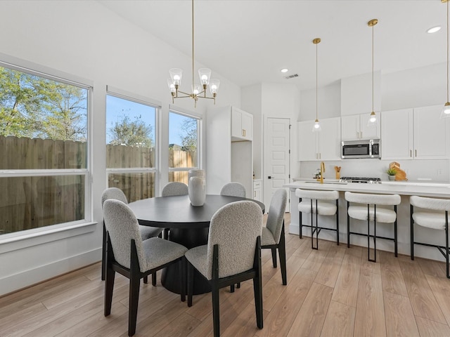 dining space with a high ceiling, sink, an inviting chandelier, and light hardwood / wood-style floors