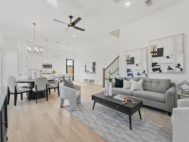 living room featuring ceiling fan with notable chandelier, light hardwood / wood-style floors, and a towering ceiling