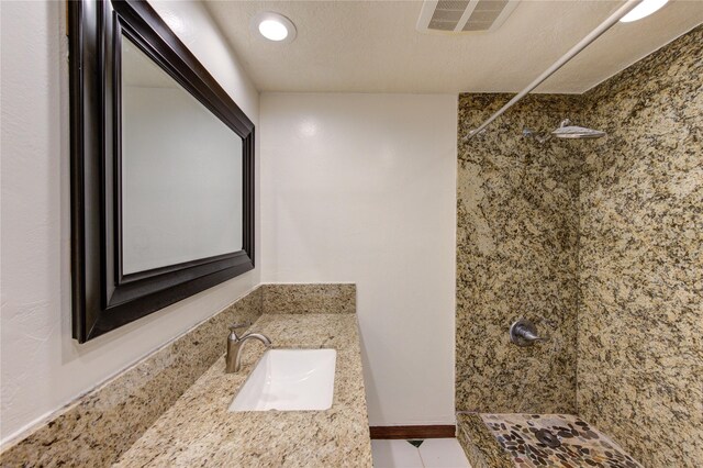 bathroom featuring a tile shower, vanity, and a textured ceiling