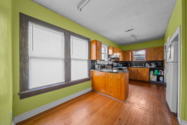 kitchen with dark wood-type flooring, range, a textured ceiling, kitchen peninsula, and white fridge