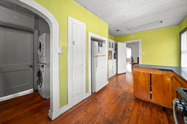 kitchen featuring stacked washer / dryer, dark hardwood / wood-style flooring, white refrigerator, range, and a textured ceiling