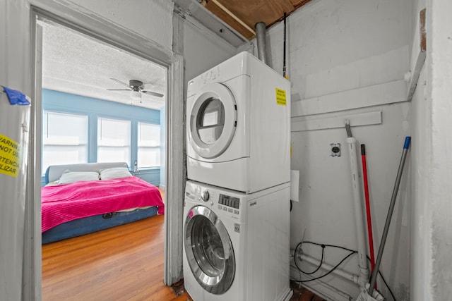 washroom with hardwood / wood-style flooring, a textured ceiling, ceiling fan, and stacked washer / dryer