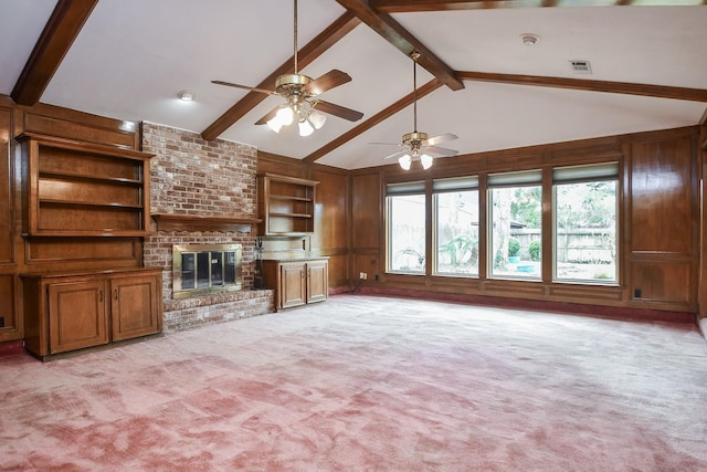 unfurnished living room featuring wooden walls, light carpet, a brick fireplace, built in shelves, and beamed ceiling